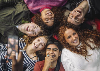 Hand of unrecognizable person photographing cheerful teenage friends having fun while lying down at park - MASF41322