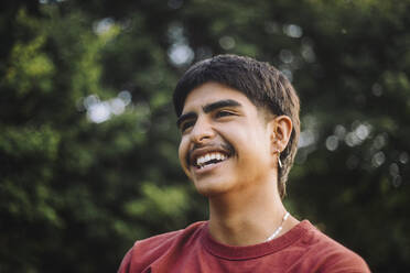 Low angle shot of a cheerful teenage boy enjoying the outdoors in a park - MASF41330