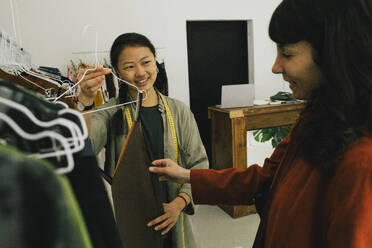 Cheerful sales team presents dress options to delighted female shopper in clothing boutique - MASF41371