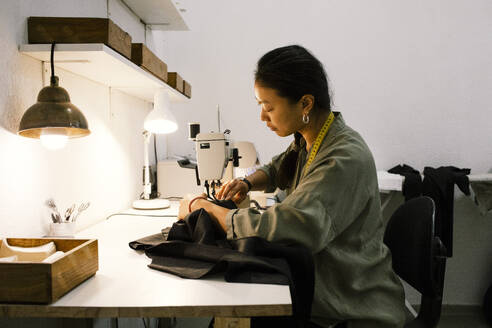 Eine junge Näherin arbeitet mit einer Nähmaschine in einem Geschäft an einem Kleid, von der Seite gesehen. - MASF41374