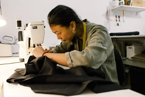 Eine gelernte Näherin konzentriert sich auf ihre Arbeit, indem sie eine Nähmaschine benutzt, um in einem Geschäft schöne Kleidungsstücke herzustellen - MASF41375