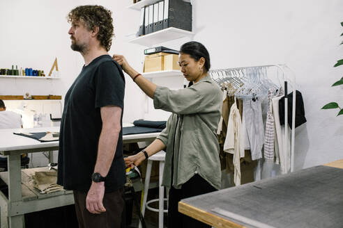 Eine Schneiderin nimmt bei einem männlichen Kunden in ihrer Werkstatt sorgfältig Maß, um sicherzustellen, dass sein Kleidungsstück perfekt sitzt - MASF41380