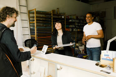 Technicians happily hand over serviced laptop to satisfied customer making payment at the store - MASF41394