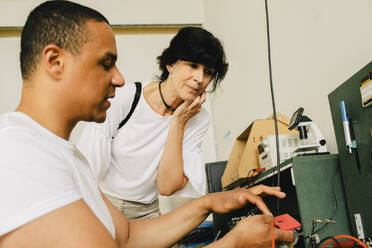 A female customer observes a male technician repairing her smartphone at a shop - MASF41402