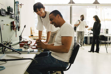 A female customer watches as a skilled male technician expertly repairs her smartphone, leaving her satisfied and happy - MASF41404