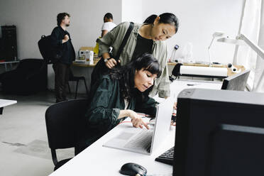 Eine Technikerin repariert einen Laptop, während sie in einem Geschäft neben einem Kunden sitzt - MASF41409