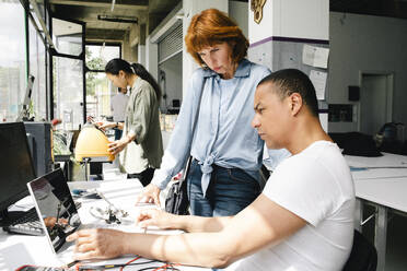 A male technician inspects a laptop while sitting next to an elderly woman at a repair shop - MASF41413