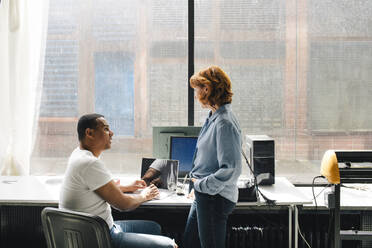 A male technician is seen discussing with a senior female customer who is standing near the desk at a repair shop - MASF41414