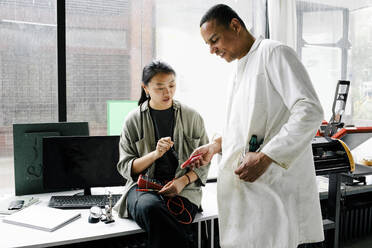 Female colleague and male technician collaborate on repairing machine part at repair shop - MASF41416