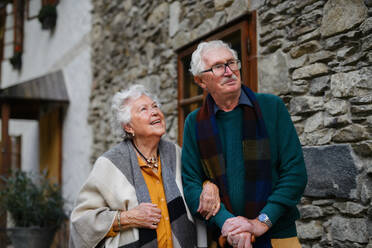 Älteres Ehepaar lächelt vor ihrem rustikalen Haus, das Freude und Zufriedenheit ausstrahlt - HPIF31678