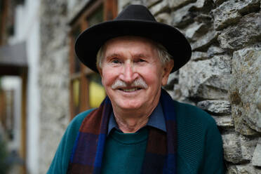Älterer Mann mit schwarzem Hut lehnt in nachdenklicher Pose an einem Haus - HPIF31686