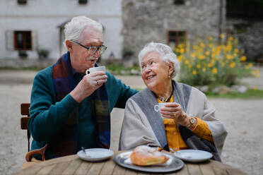 Elderly couple relishing coffee and cake while basking in the sun at an outdoor cafe - HPIF31690