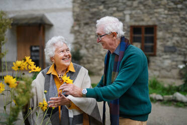 Ein lächelndes älteres Paar genießt einen malerischen Herbstspaziergang und hält an, um mit den leuchtenden Blüten zu posieren - HPIF31697