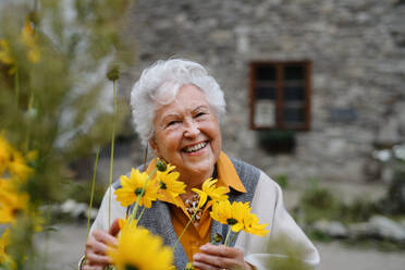 A joyful elderly woman stands outdoors, posing with a bouquet of flowers and a smile on her face. - HPIF31703