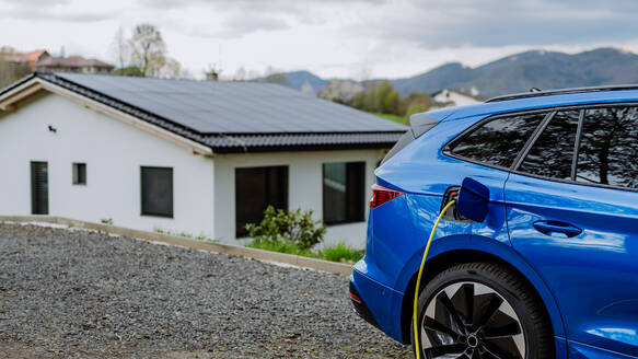 A close-up of an electric car charging in front of a residential home. - HPIF31705