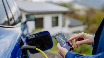 A businessman checks the charging status of his electric car using his phone in a close-up shot - HPIF31719