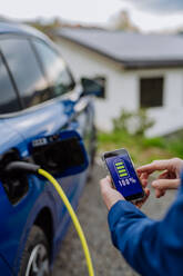 Ein Geschäftsmann überprüft den Ladestatus seines Elektroautos mit seinem Handy in einer Nahaufnahme - HPIF31720