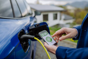 Ein Geschäftsmann überprüft den Ladestatus seines Elektroautos mit seinem Handy in einer Nahaufnahme - HPIF31721