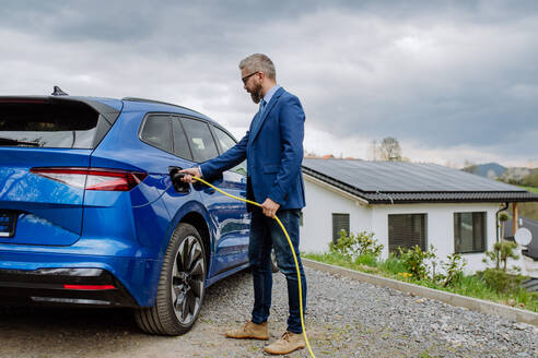 A seasoned executive charges his new electric vehicle with a power supply cable - HPIF31728