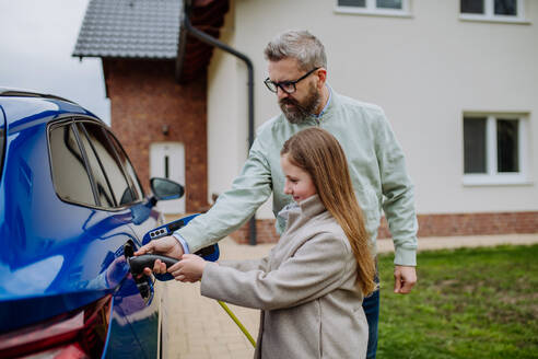 Ein Vater und seine Tochter laden ihr umweltfreundliches Elektrofahrzeug auf und leisten damit einen Beitrag zu einer nachhaltigen Zukunft - HPIF31748