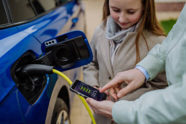 A father and daughter inspect the charging status of their electric car using a mobile phone in a close-up shot - HPIF31750