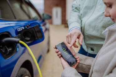 A father and daughter inspect the charging status of their electric car using a phone in a close-up shot - HPIF31751