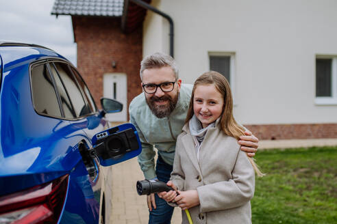 Ein Vater und seine Tochter laden ihr umweltfreundliches Elektrofahrzeug auf und fördern damit nachhaltige Verkehrspraktiken - HPIF31752