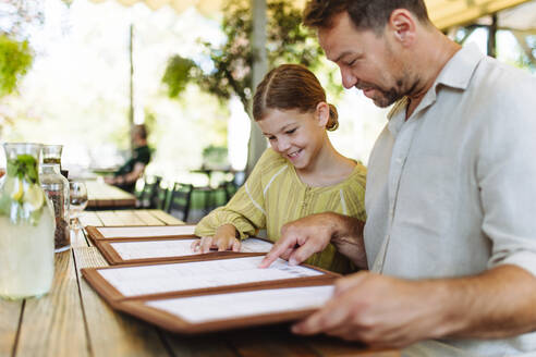 Ein Vater und seine Tochter wählen Speisen und Getränke aus der Speisekarte aus, während sie ein Familienessen in einem Restaurant genießen - HPIF31765