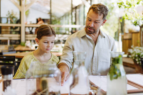 Ein Vater und seine Tochter stöbern in der Speisekarte und entscheiden, was sie während ihres Familienessens in einem Restaurant essen und trinken wollen - HPIF31767