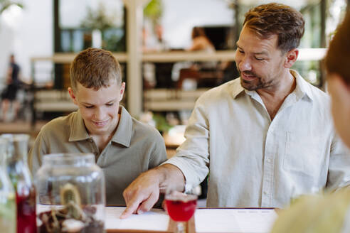 Vater und Sohn sehen sich die Speisekarte an und treffen eine Auswahl für ihr Familienessen in einem gemütlichen Restaurant - HPIF31769