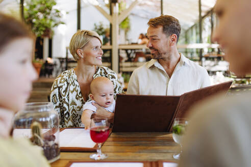 Eine dreiköpfige Familie, darunter ein Baby, sieht sich die Speisekarte an und wählt Speisen und Getränke während eines Restaurantbesuchs aus - HPIF31773