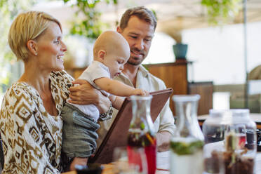 A young family enjoys a delicious meal together at a restaurant, with their adorable baby joining in on the fun - HPIF31776