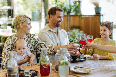 Eine glückliche Familie, die mit ihren kleinen Kindern und einem Baby in einem familienfreundlichen Restaurant ein festliches Essen genießt und mit Gläsern anstößt - HPIF31781