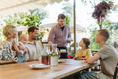 Ein Kellner serviert einer glücklichen Familie ein köstliches Essen in einem gemütlichen Restaurant - HPIF31785