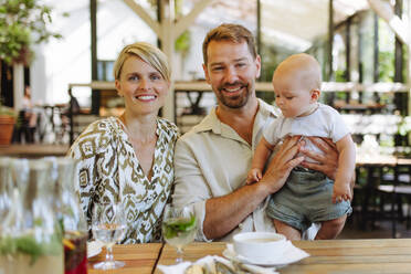 Eine Familie, die eine Mahlzeit in einem Restaurant genießt, mit einem hungrigen Baby, das eifrig Suppe isst - HPIF31786