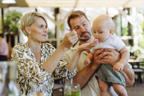 Parents enjoying a family dinner at a restaurant while feeding their little one - HPIF31787