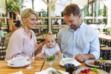 A happy family enjoying a meal together at a restaurant, with their little one comfortably seated in a high chair - HPIF31788
