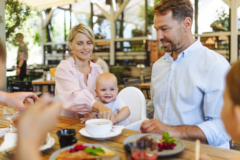Eine glückliche Familie, die eine Mahlzeit in einem Restaurant genießt, während ihr kleiner Sohn bequem in einem Hochstuhl sitzt - HPIF31789