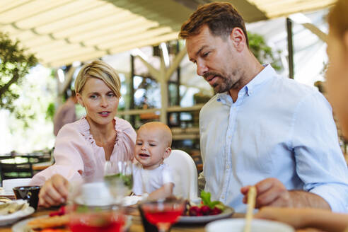 Eine Familie, die gemeinsam in einem Restaurant isst, mit einem hungrigen Baby in einem Hochstuhl, das eifrig isst - HPIF31790