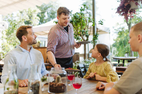 Ein Kellner bringt köstliche Gerichte zu einer Familie, die in einem Restaurant zu Abend isst - HPIF31791