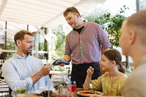 Ein Kunde bezahlt sein Mittagessen in einem Restaurant kontaktlos mit einer Karte und einem Kartenlesegerät - HPIF31795
