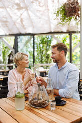 Portrait of beautiful couple in a restaurant, on a romantic date. Husband and wife are clinking champagne glasses, making a toast at restaurant patio. - HPIF31798