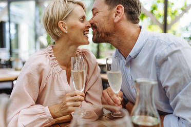 Close up of beautiful couple in a restaurant, on a romantic date. Wife and husband kissing, having a romantic moment at restaurant patio. - HPIF31801