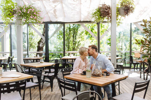 Ein verliebtes Paar, das einen romantischen Moment auf einer Restaurantterrasse verbringt und die Gesellschaft des anderen bei einem Kuss genießt - HPIF31804