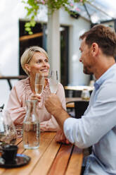 Portrait of beautiful couple in a restaurant, on a romantic date. Husband and wife are clinking champagne glasses, making a toast at restaurant patio. - HPIF31806