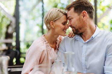 Ein verliebtes Paar genießt einen romantischen Moment, während es auf der Terrasse eines Restaurants speist, die Stirne berührt und die Gesellschaft des anderen genießt - HPIF31810