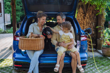 Eine fröhliche Familie wartet darauf, dass ihr Elektroauto aufgeladen wird, bevor sie zu einem Picknick aufbricht - HPIF31830