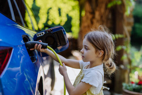 Ein junges Mädchen lädt ein Elektroauto mit einem Stromkabel auf und leistet damit einen Beitrag zu einer nachhaltigen Zukunft - HPIF31834