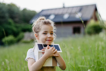Ein junges Mädchen hält stolz ein Modell eines mit Solarzellen ausgestatteten Hauses in die Höhe, das ein Engagement für Nachhaltigkeit und erneuerbare Energien symbolisiert. - HPIF31837