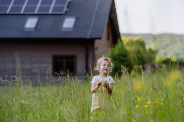 Ein junges Mädchen steht vor dem solarbetriebenen Haus ihrer Familie und wirbt für nachhaltiges Leben und erneuerbare Energien. - HPIF31843